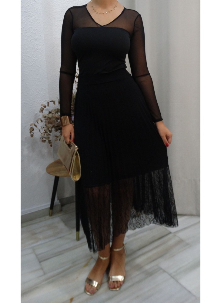 Modelo posando con falda plisada en color negro con cinturilla elástica y bajo de encaje, combinada con camisa de transparencias