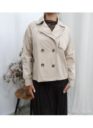 Modelo posando con gabardina corta de color beige, diseño de doble botonadura y solapas, combinada con jeans