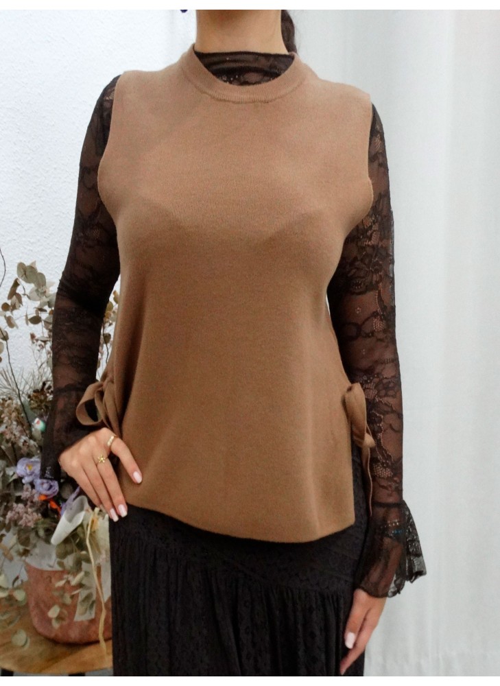 Modelo posando con chaleco cerrado en color camel, apertura en los lados con lazos en el mismo tono.