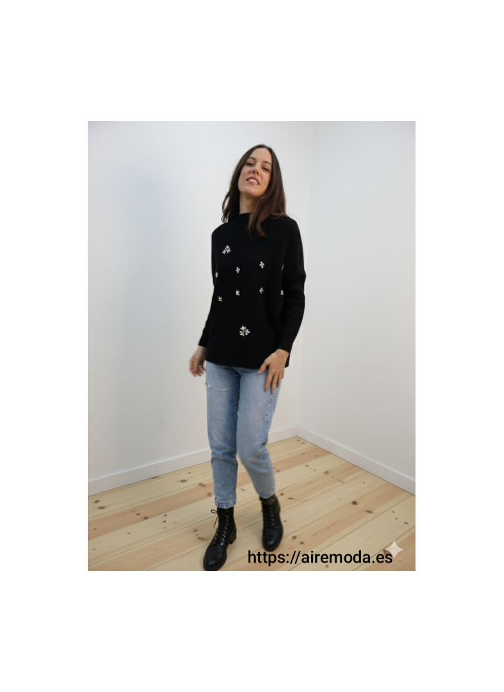 Modelo posando con jersey negro con detalles de pedrería brillantes y cuello redondo, combinado con jeans claros.