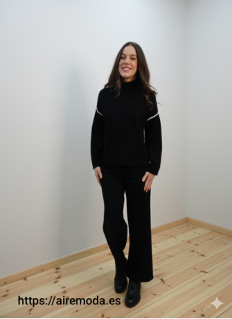 Modelo posando con jersey de punto negro de cuello perkins y adorno de raya blanca en espalda y parte superior de las mangas