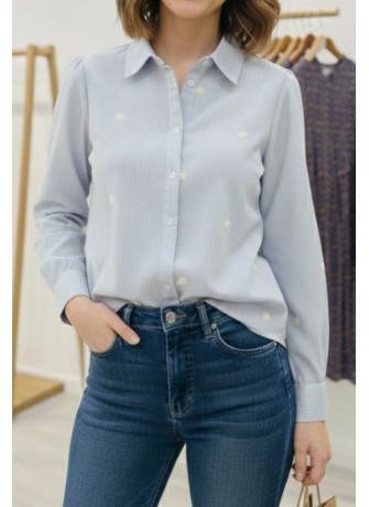 Modelo posando con camisa de manga larga azul claro, con detalles de flores pequeñas bordadas, combinada con jean