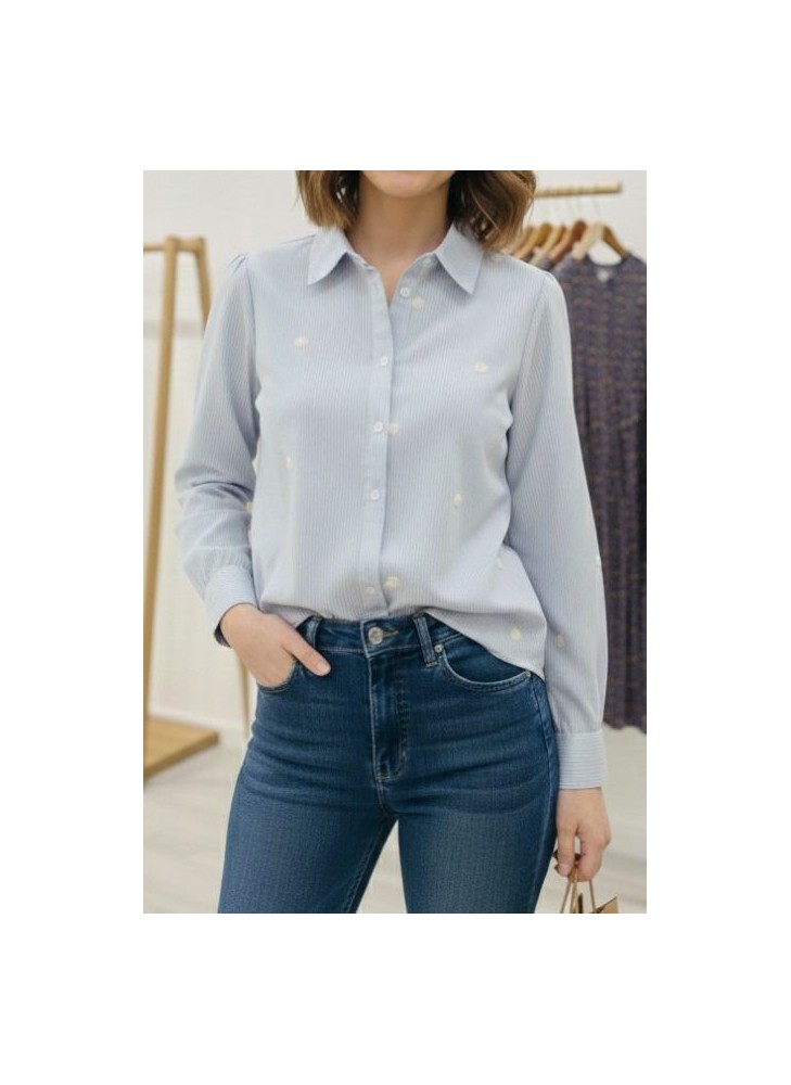 Modelo posando con camisa de manga larga azul claro, con detalles de flores pequeñas bordadas, combinada con jean