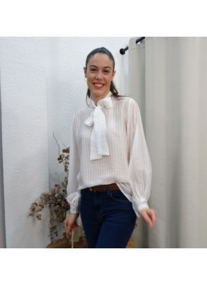 Modelo luciendo camisa blanca semitransparente para mujer con cuello de lazada y estampado de rayas verticales sutiles