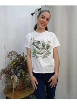 Modelo posando con  camiseta blanca de manga corta con estampado central de zapatillas de lona verdes y mariposas