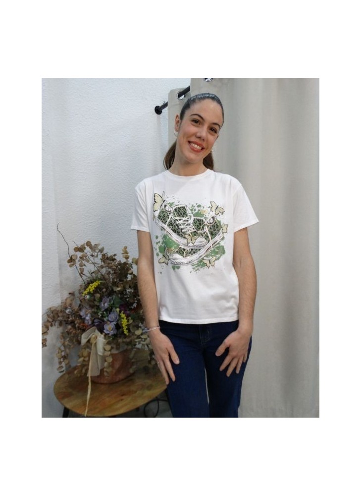 Modelo posando con  camiseta blanca de manga corta con estampado central de zapatillas de lona verdes y mariposas