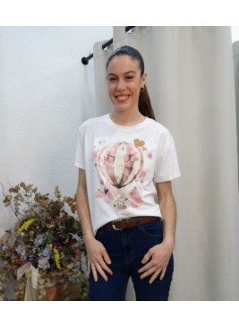 Modelo posando con camiseta blanca con ilustración de globo aerostático rosa y detalles de flores y corazones dorados