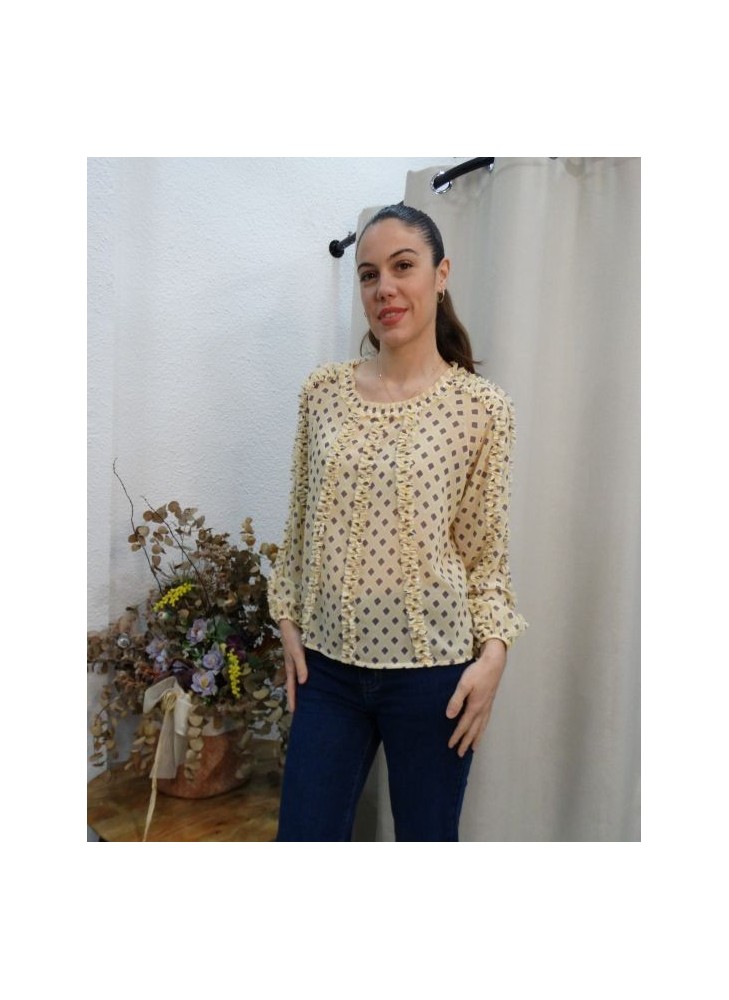 Mujer posando con blusa de gasa color crema con estampado de rombos y detalles de volantes verticales