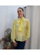 Modelo luciendo camisa de gasa semitransparente en color amarillo vibrante con lazo grande en el cuello y mangas abullonadas.