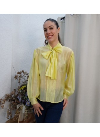 Modelo luciendo camisa de gasa semitransparente en color amarillo vibrante con lazo grande en el cuello y mangas abullonadas.
