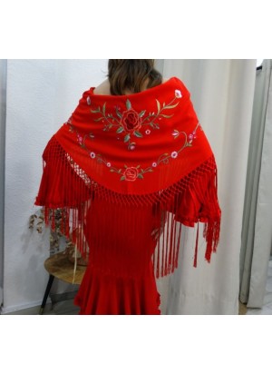 Modelo luciendo mantón de flamenca en color rojo con bordados florales en tonos verde y rosa, detalle de flecos largos.
