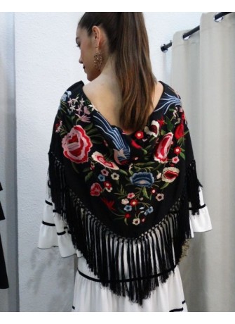 Modelo posando con mantón de flamenca color negro con bordados florales en tonos rosa, rojo y azul
