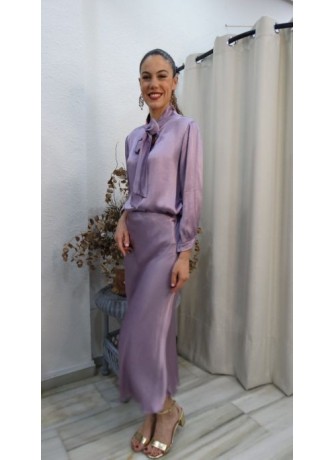 Modelo luciendo un conjunto satinado de dos piezas en color lavanda con blusa de lazada y falda midi