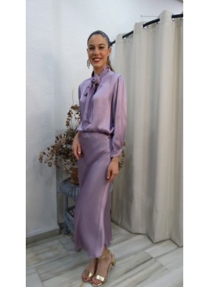 Modelo luciendo un conjunto satinado de dos piezas en color lavanda con blusa de lazada y falda midi